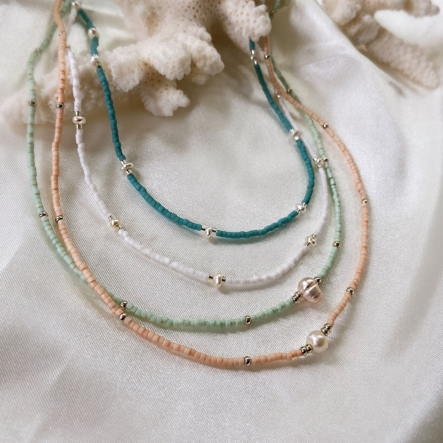 woman layering mint and turquoise dainty beaded necklaces