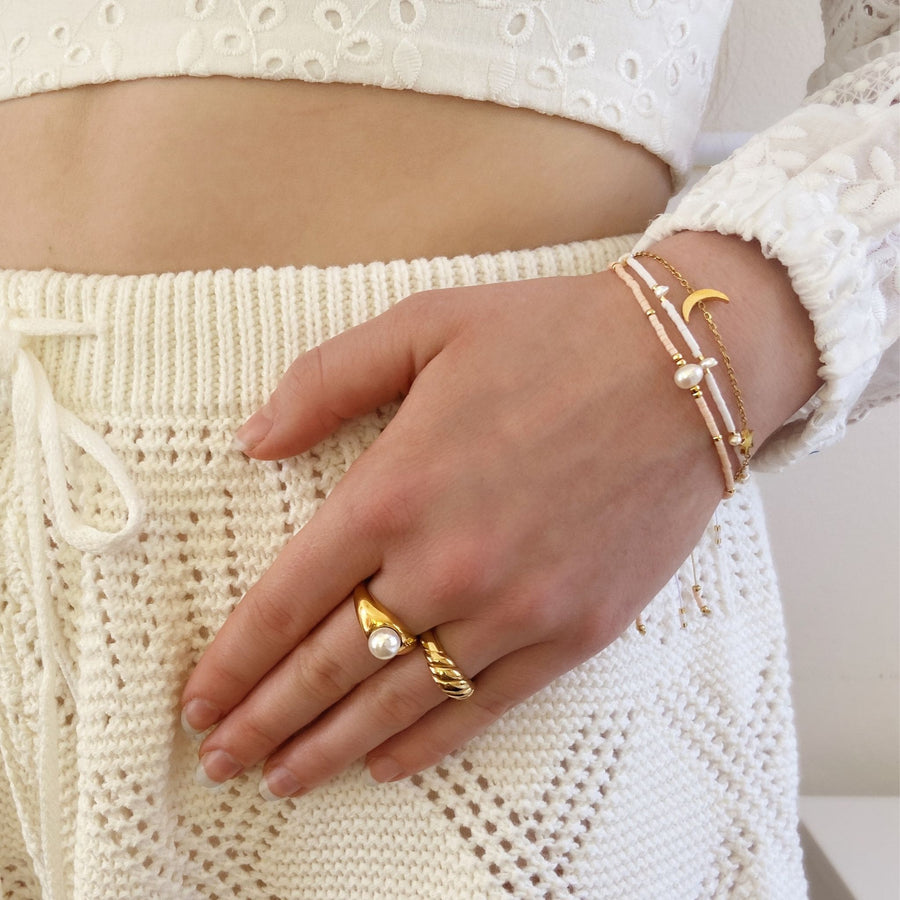 hand on white knit shorts with gold rings and dainty beaded pearl bracelets