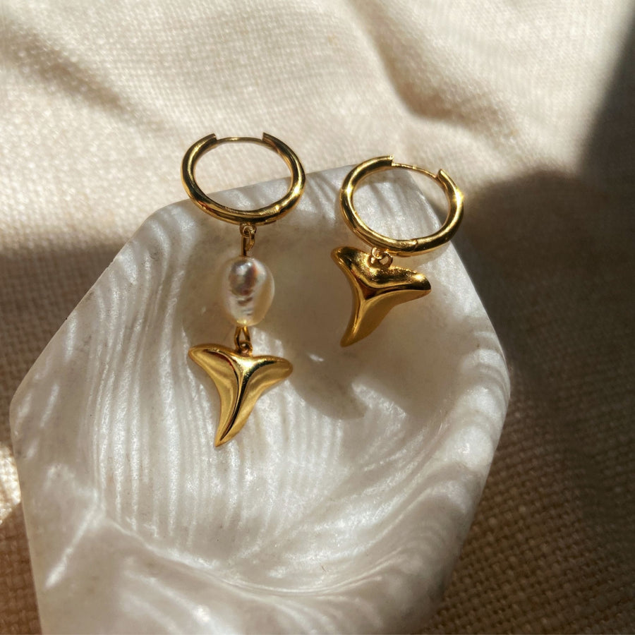 gold shark tooth earrings on marble dish