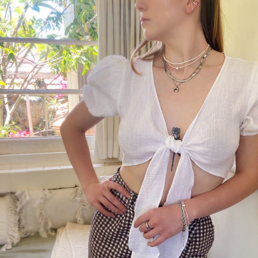 woman wearing front tie white top and gingham pants, with silver stacking jewellery